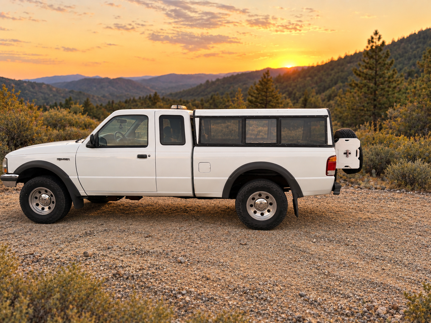 White Ford Ranger with TrailSwing spare tire carrier, driver-side profile on a gravel trail